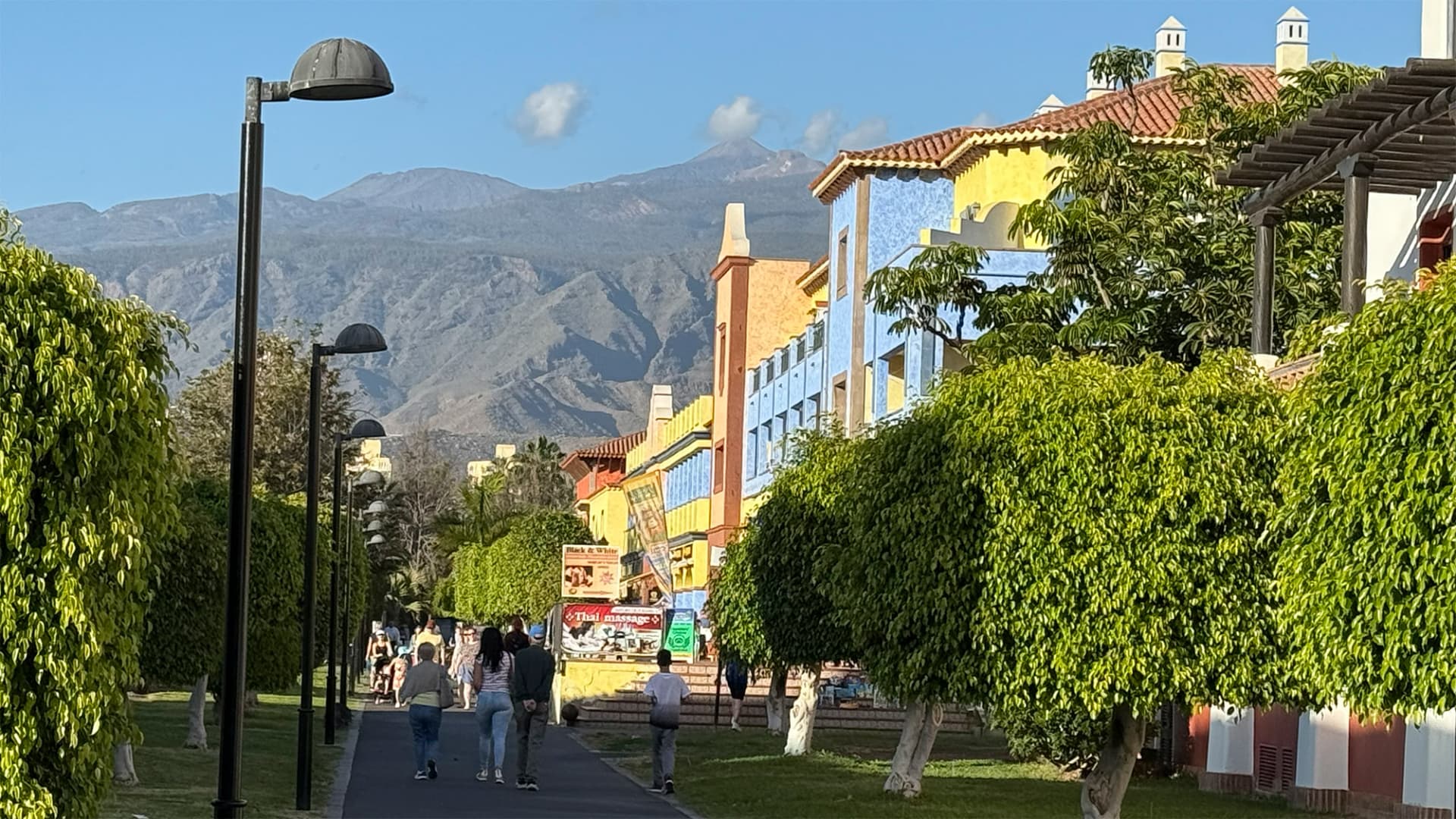Paseo ajardinado del sur de Tenerife con edificios de colores y la silueta del Teide al fondo