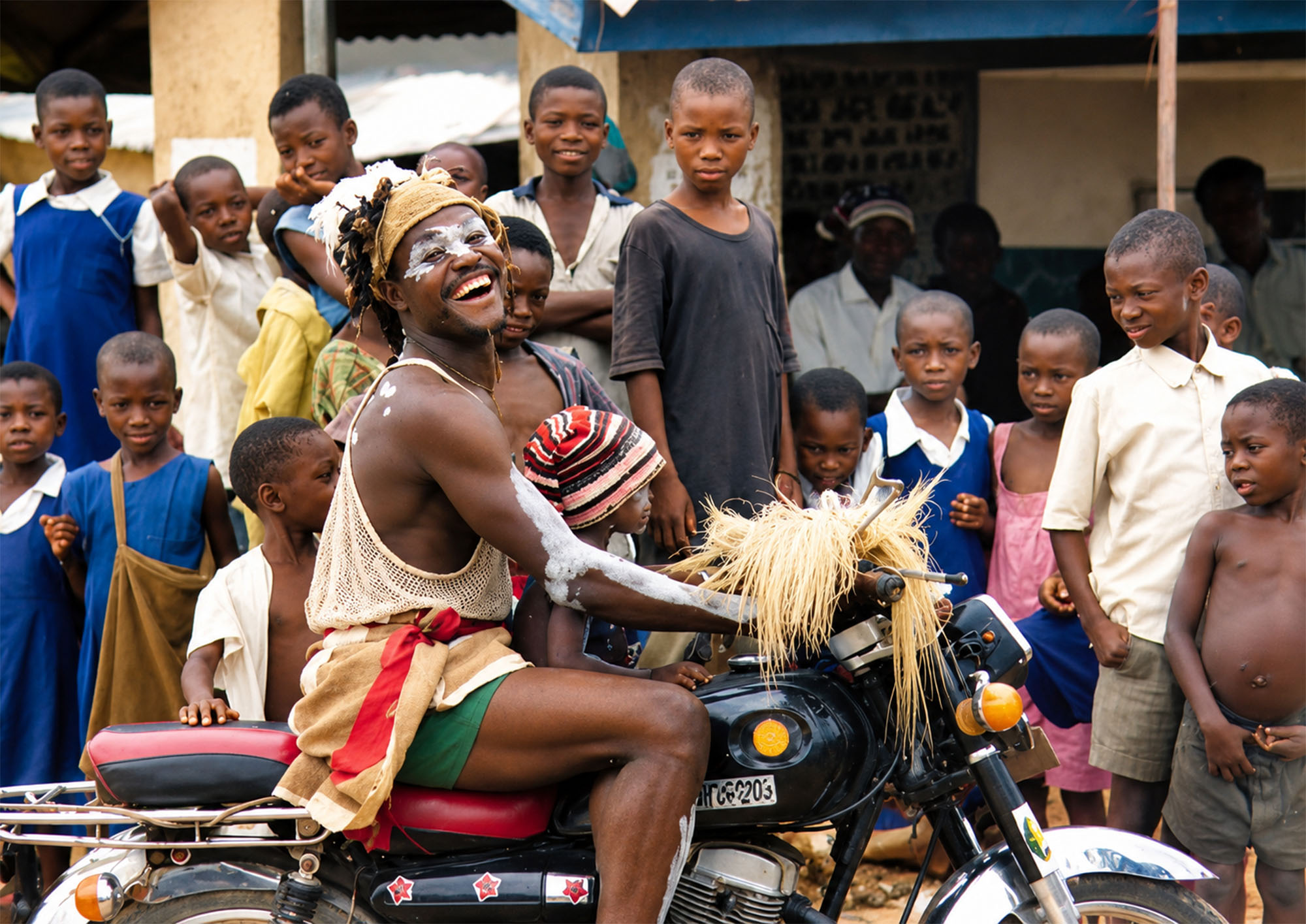 Danzante sonriente sobre una motocicleta rodeado de niños en Port Harcourt durante la Travesía Nigeriana