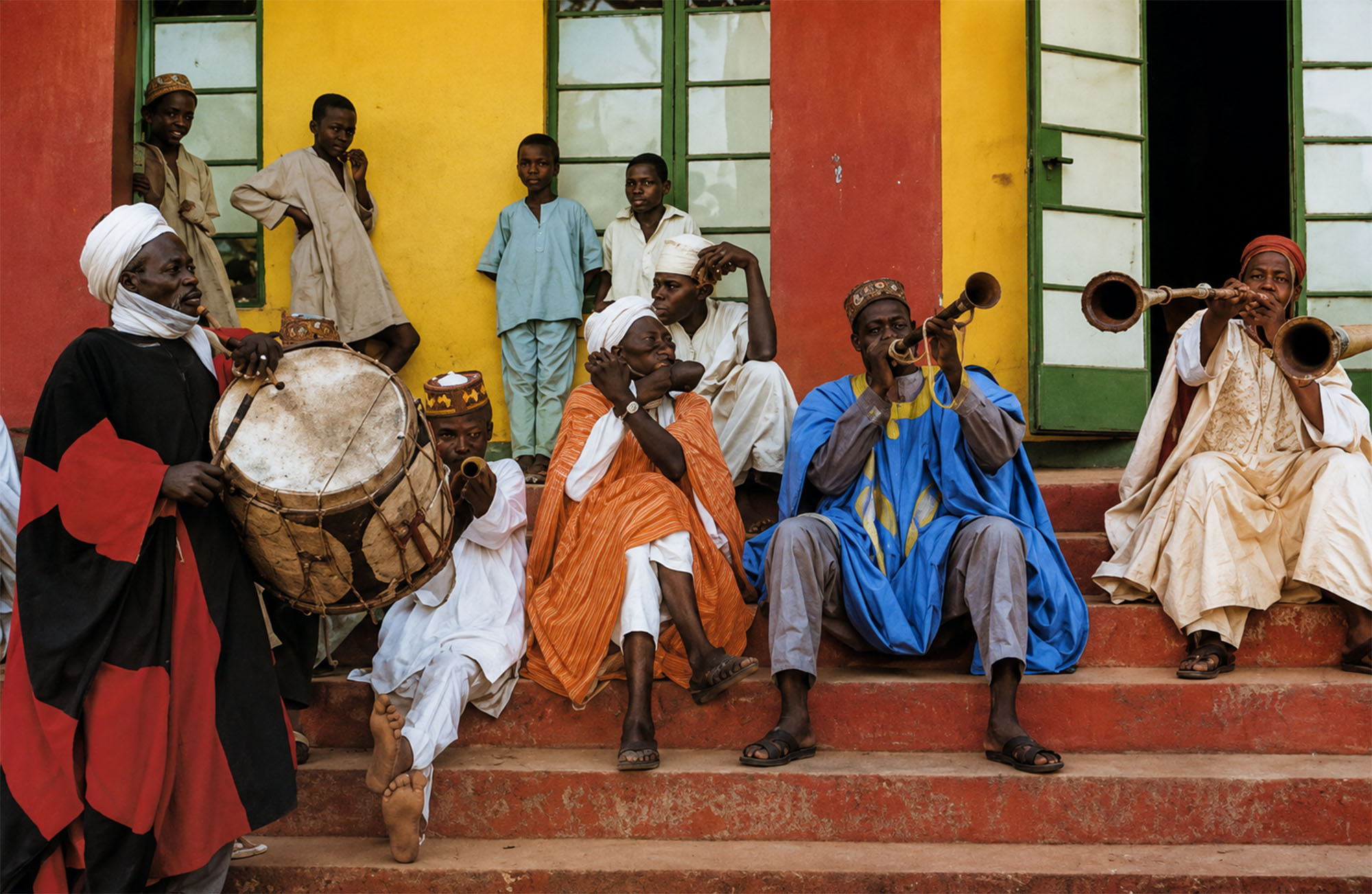 Músicos con tambor y trompetas tradicionales sentados en una escalinata de fachada colorida en Sokoto durante la Travesía Nigeriana