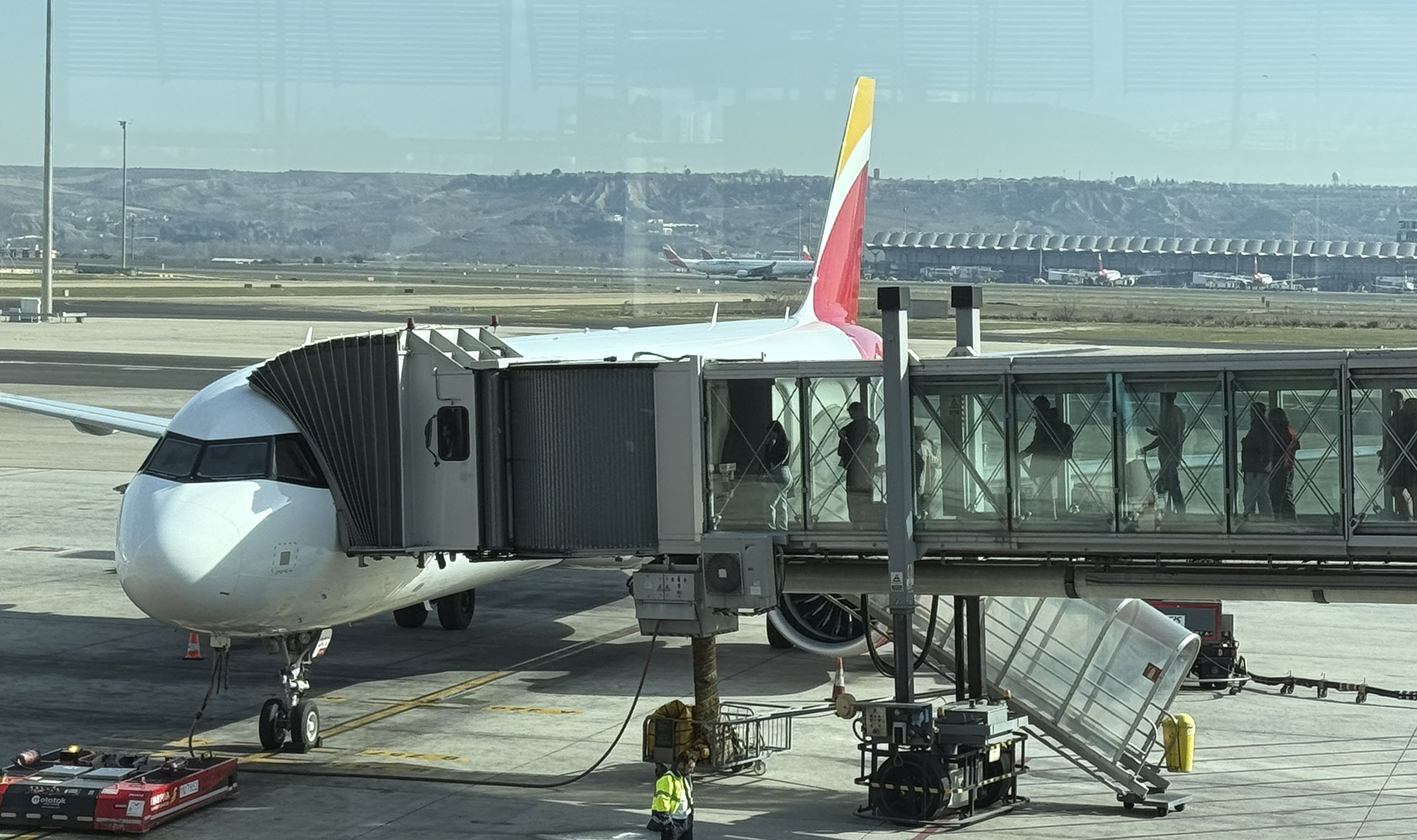 Avión de línea conectado a una pasarela de embarque con colinas al fondo