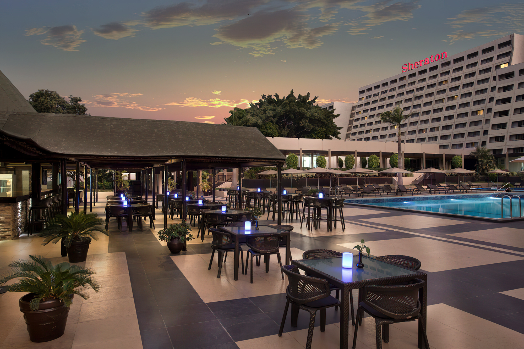 Terraza del hotel Sheraton de Abuya al atardecer con piscina, toldos y mesas iluminadas durante la Travesía Nigeriana